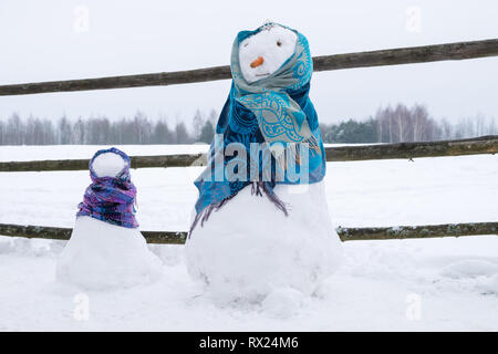 Zwei niedliche Schneemänner in Schals auf schneebedeckten Feld gewickelt. Stockfoto
