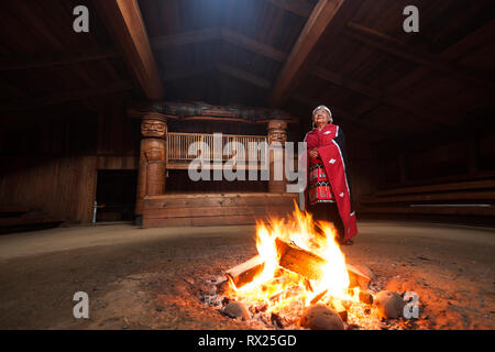 Eine erste Nationen Elder gekleidet in ihren traditionellen Insignien steht neben einem Feuer im bighouse im Dorf Oweekeno. Wuikinuxv, Flüsse, Einlass, Br Stockfoto