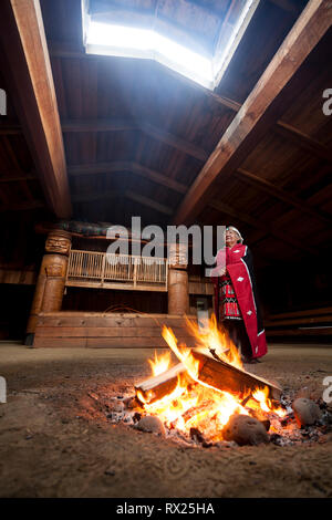 Eine erste Nationen Elder gekleidet in ihren traditionellen Insignien steht neben einem Feuer im bighouse im Dorf Oweekeno. Wuikinuxv, Flüsse, Einlass, Br Stockfoto