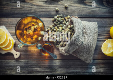 Gesunde Kamille Tee Tasse, hessische Beutel der trockenen Daisy Blumen, Honig jar und Zitronenscheiben. Ansicht von oben. Stockfoto