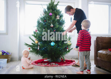 Vater schmückt den weihnachtsbaum, während er mit Kindern zu Hause steht Stockfoto