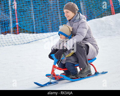 Im Winter, glückliche Mutter und Sohn 3 Jahre alt a Snow Scooter vom Berg Fahrt in reinen, weißen Schnee. Stockfoto