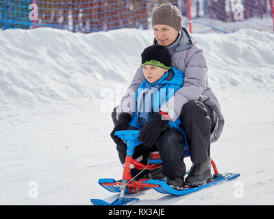 Im Winter, glückliche Mutter und Sohn 7 Jahre alt a Snow Scooter vom Berg Fahrt in reinen, weißen Schnee. Stockfoto