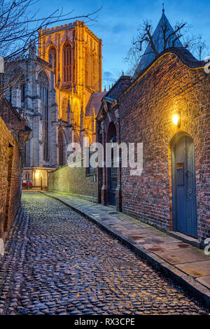 Kleine Straße mit Kopfsteinpflaster in York nachts mit dem berühmten Münster in der Rückseite Stockfoto