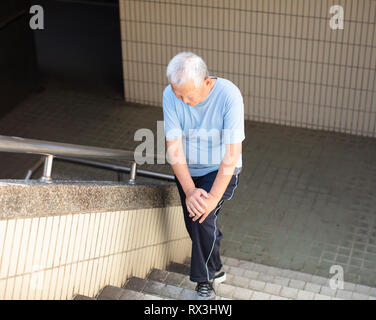 Männliche ältere Leiden unter Knieschmerzen auf Treppe Stockfoto