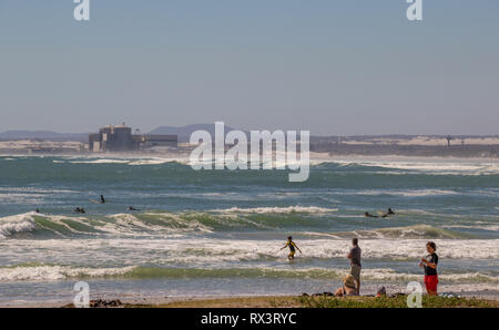 Kapstadt, Südafrika - Unbekannter Badende im Meer schwimmen Melkbosstrand mit dem Kernkraftwerk Koeberg droht in den Hintergrund Stockfoto