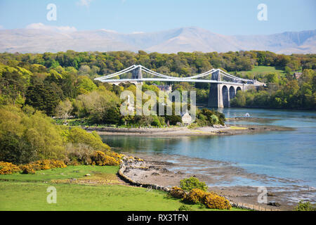 Die menai Suspension Bridge und Kirche Insel im Vordergrund bei Flut auf Anglesey im Norden von Wales. Die Berge von Snowdonia im Hintergrund. Stockfoto