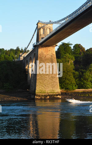 Ein Motorboot fährt auf den Menaistraße unter der Menai Suspension Bridge neben Anglesey Stockfoto