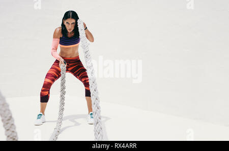 Fitness-Frau, die Krafttraining mit Kampfseilen macht. Athletische Frau, die mit Kampfseilen trainiert. Stockfoto