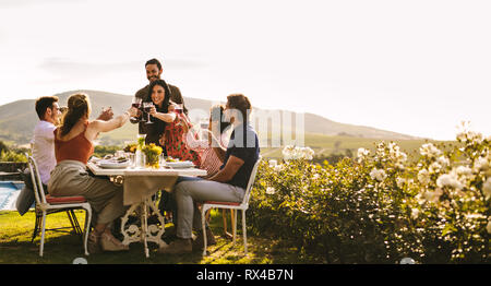 Paare, die ein Toast mit Freunden am Tisch sitzen während der Party. Gruppe von Freunden feiern einen besonderen Anlass mit Getränken. Stockfoto