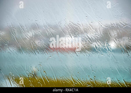 Fallen Regen erzeugen Streifenmuster auf dem Glas ein Fenster an einem regnerischen Tag in Hafnarfjordur, Island, mit dahinter kaum erkennbar die blurre Stockfoto