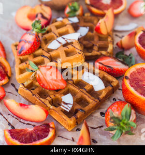 Waffeln mit Erdbeeren, Kokos, Pflaume und orange mit Schokolade Stockfoto