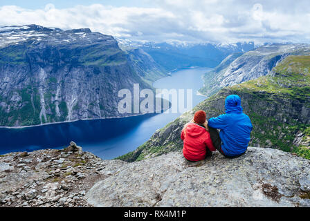 Paar sitzt auf Felsen und blickt auf die Berge in der Nähe von trolltunga. Beliebte Touristenattraktion. Ringedalsvatnet - See in der Gemeinde Odda in Hordalan Stockfoto