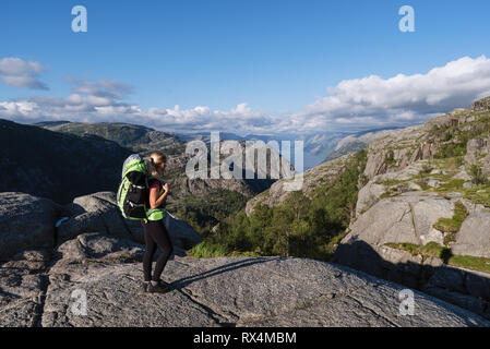 Touristen mit einem Rucksack auf Pathway Pulpit Rock. Blonde Mädchen in einem Mountain Trek. Blick auf den Lysefjord, Norwegen Stockfoto