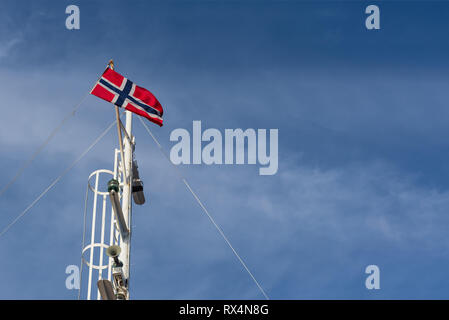 Norwegische Flagge auf einem Fahnenmast vor blauem Himmel. Sonniges Wetter in Norwegen Stockfoto