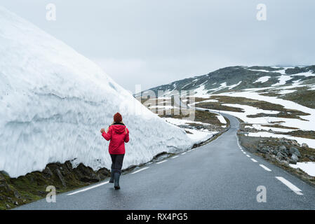 Bjorgavegen - verschneite Straße in Norwegen. Fröhliches Mädchen läuft auf einem Berg Straße in der Nähe einer Wand aus Schnee. Schwere nördlichen Landschaft Stockfoto