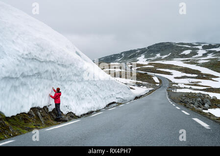 Bjorgavegen - verschneite Straße in Norwegen. Fröhliches Mädchen auf einem Berg Straße in der Nähe einer Wand aus Schnee. Schwere nördlichen Landschaft Stockfoto