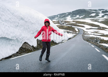 Bjorgavegen - verschneite Straße in Norwegen. Fröhliches Mädchen auf einem Berg Straße in der Nähe einer Wand aus Schnee. Schwere nördlichen Landschaft Stockfoto