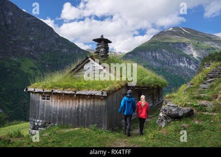 Kagefla - historische Bergbauernhöfen auf die Berghänge entlang der Geiranger Fjord. Touristische Attraktion von Norwegen. Ein paar Reisende, tr Stockfoto