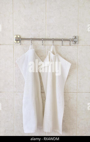 Zwei weiße Frottee Handtücher auf einem Kleiderbügel auf dem Hintergrund einer Wand von keramischen Fliesen. Stockfoto