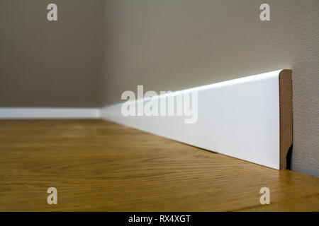 Holz- oder Kunststoff Weiß, Sockel Installation in großen leeren Raum auf Holzboden und weiß verputzt verputzten Wänden Hintergrund. Details im Innenraum. Stockfoto