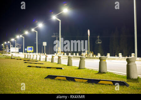 Leeren Parkplatz auf grünen Rasen hell von Laternen entlang der Straße am dunklen Nachthimmel Kopie Raum Hintergrund beleuchtet. Stockfoto