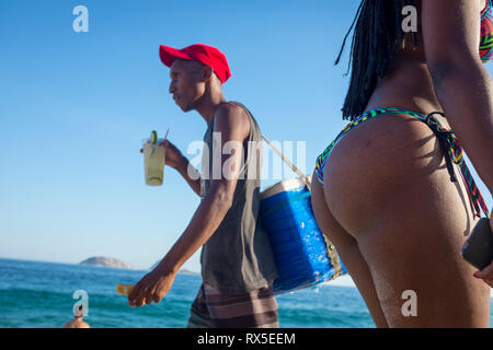 RIO DE JANEIRO - Februar 5, 2017: Ein Strand Anbieter Getränke ein Caipirinha Cocktail, als Er übergibt einen beachgoers in Bikinis am Strand von Ipanema. Stockfoto