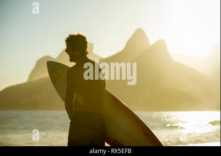 RIO DE JANEIRO - 20. MÄRZ 2017: Eine junge brasilianische Surfer steht auf dem Boardwalk in Arpoador, der beliebten Surf Point und den Sonnenuntergang genießen. Stockfoto