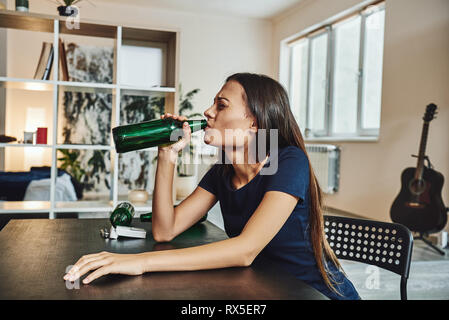 Deprimiert, geschiedene Frau, die alleine zu Hause sitzen und trinken Bier aus der Flasche, da es Probleme bei der Arbeit und Mühen in Beziehungen. Sozial- und Stockfoto