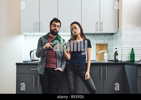 Junge Frau und ihren Mann stehen in der Küche halten Bierflaschen und Anstoßen. Sie beide haben Depressionen, beide leiden unter Alkohol hinzufügen Stockfoto