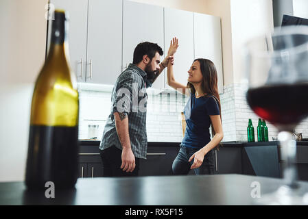 Portrait von Mann und Frau in Streit und Kämpfe in der Küche. Eine Flasche und ein Glas Wein auf dem Tisch. Selektiver Fokus Stockfoto