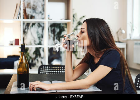 Deprimiert, geschiedene Frau alleine zu Hause sitzen und trinken ein Glas Rotwein, da es Probleme bei der Arbeit und Mühen in Beziehungen. Sozial- und Stockfoto