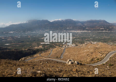 Land straße aus den Bergen in Lassithi Hochebene, landwirtschaftliche Teil der Insel, in der Mitte befindet. Felder mit den Bergen im Hintergrund. B Stockfoto