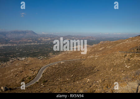 Land straße aus den Bergen in Lassithi Hochebene, landwirtschaftliche Teil der Insel, in der Mitte befindet. Felder mit den Bergen im Hintergrund. B Stockfoto