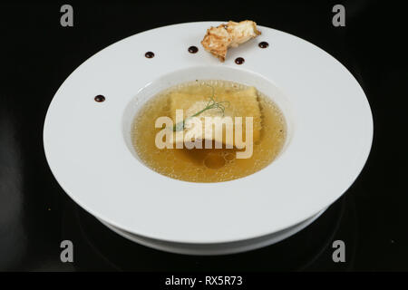 Minimalistischer Servieren von Essen, weiß transparent Hühnerbrühe in einen Teller mit Reis, Käse und Knödel, dekoriert mit Erbse germ Stockfoto