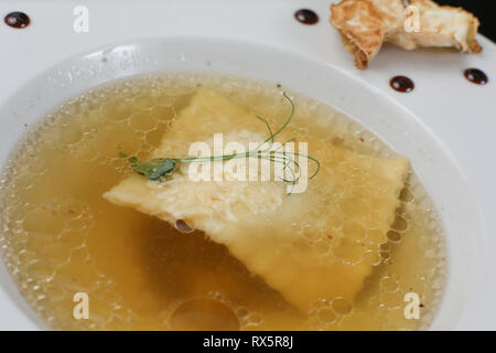 Minimalistischer Servieren von Essen, weiß transparent Hühnerbrühe in einen Teller mit Reis, Käse und Knödel, dekoriert mit Erbse germ Stockfoto