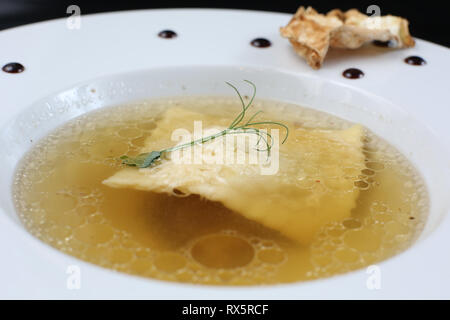 Minimalistischer Servieren von Essen, weiß transparent Hühnerbrühe in einen Teller mit Reis, Käse und Knödel, dekoriert mit Erbse germ Stockfoto