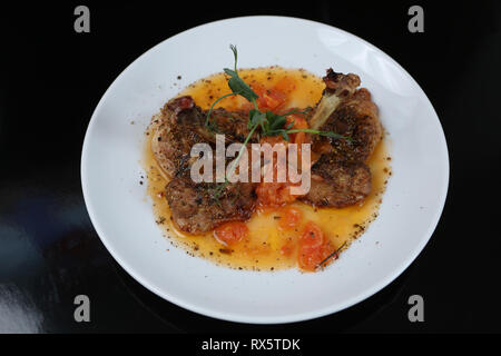 Fried Chicken leg mit Tomaten und Gewürzen auf einer Platte Stockfoto
