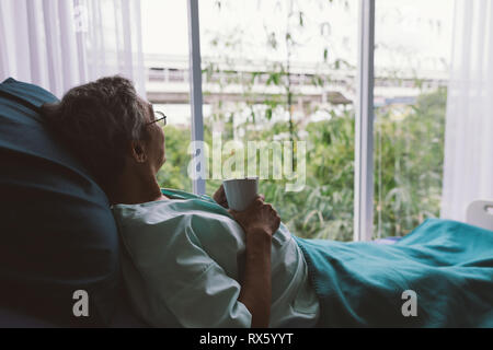 Älterer Mann auf einem Krankenhausbett allein in einem Zimmer, durch das Krankenhaus Fenster. Ältere Patienten Stockfoto