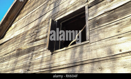 Eine Scheune mit einem Fenster. Die alten hölzernen Schuppen an der Außenseite. Blick auf die retro Bauernhaus Wand von unten nach oben. Vintage Szene mit einem beschädigten Gebäude aus Holz. Stockfoto