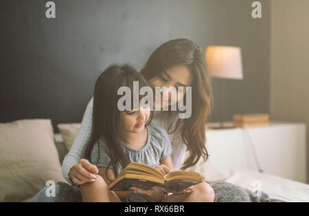 Mutter und Tochter lesen Buch zu Hause im Schlafzimmer Stockfoto