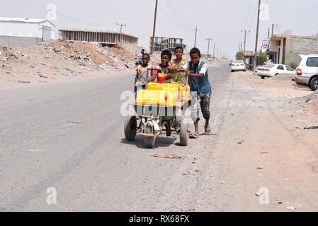 Aden, Jemen. 8 Mär, 2019. Jemenitische Kinder drücken Sie eine Schubkarre mit Flaschen Trinkwasser in Aden, Jemen, März 8, 2019 geladen. Tausende von jemenitischen Kinder haben auf die Straßen als Folge der wachsenden militärischen Konflikt, der zwischen der jemenitischen Regierung und der Rebellen Houthi im Jahr 2015 brach geschoben. Die Anzahl der Straßenkinder steigt immer noch auf einer täglichen Grundlage wie Kämpfe, Erweiterung mehr Provinzen in den verarmten arabischen Land inmitten der Mangel an politischen Lösungen zu Ende der 4-jährigen Bürgerkrieg. Credit: Murad Abdo/Xinhua/Alamy leben Nachrichten Stockfoto