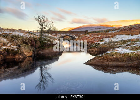 Pont Ar Bavaria, Elan Tal, Wales verschneite Szene des Afon Elan durch eine Brücke fliesst im Winter mit einsamen Baum im Wasser und am frühen Morgen Sun Li wider Stockfoto