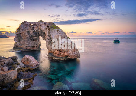 Es Pontas auf Mallorca mit Boot in der Nähe des Mittelmeers verankert. Sunrise mit Yacht und rock Arch in der Nähe von Santanyi Mallorca Stockfoto