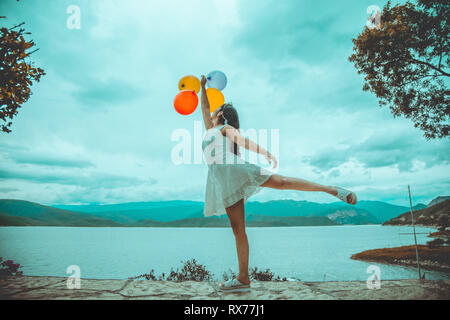 Junge Frau mit Ballons mit einem See im Hintergrund Stockfoto