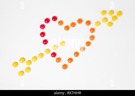 Form Herz mit Pfeil durchbohrt, als Symbol der Liebe - von bunten süßen Bonbons - Ansicht von oben - weißer Hintergrund gemacht Stockfoto