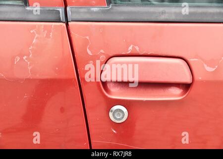 Fading Autolack - abblätternde Farbe Oberfläche in einem 20 Jahre alten Europäischen rotes Auto. Stockfoto