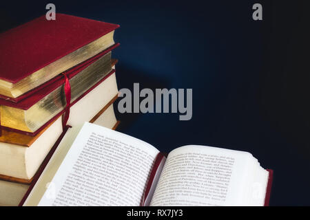 Stapel alter Bücher und ein offenes Buch gegen einen dunkelblauen Hintergrund mit Speicherplatz für eigene Text kopieren Stockfoto