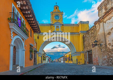 Das Agua Vulkan durch die ersten Sonnenstrahlen für SUNRISE beleuchtet mit der Hauptstraße von Antigua Stadt und seinen gelben Bogen, Guatemala, Mittelamerika. Stockfoto