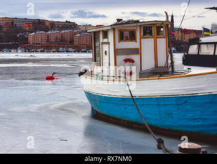 Kleines Fischerboot mit blauem Rumpf auf einem gefrorenen Fluss im Winter günstig Stockfoto